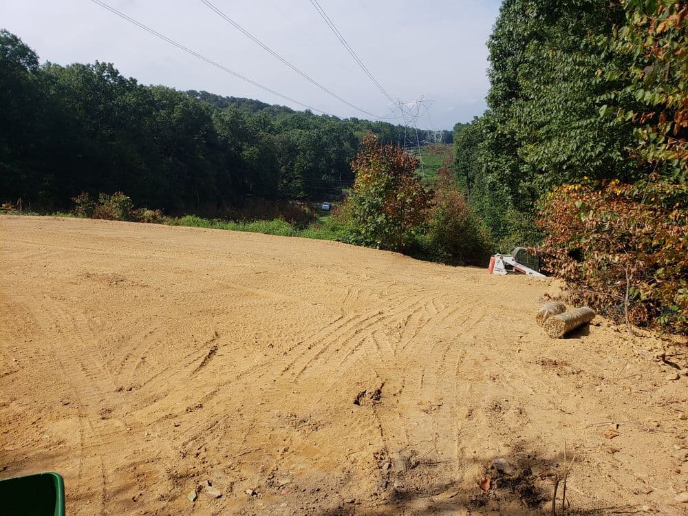Cleared construction site with freshly leveled dirt and surrounding trees in a rural landscape.