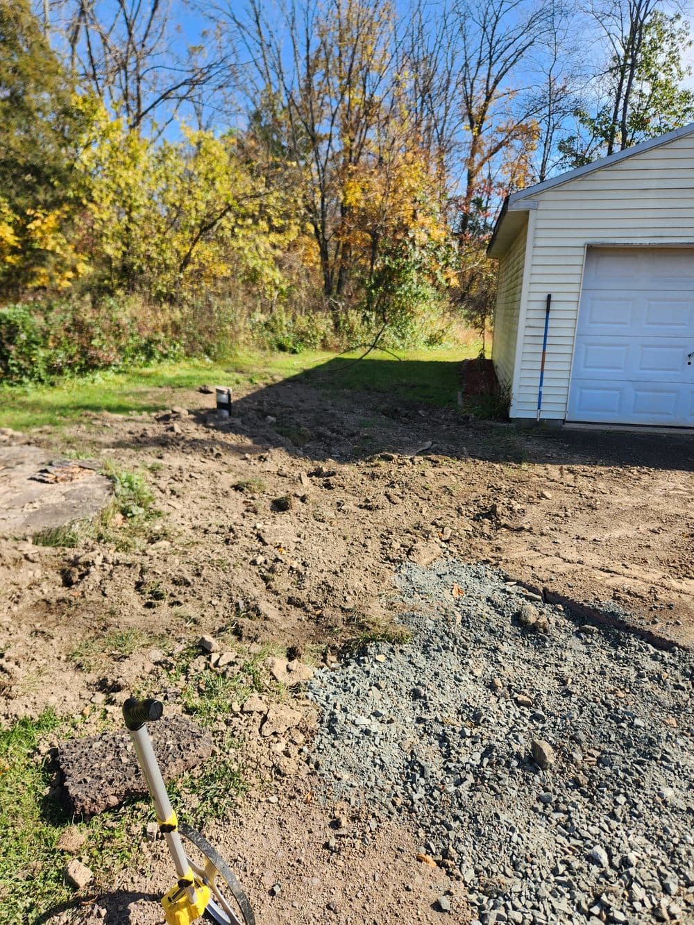 Autumn yard renovation with cleared dirt patch and garage, surrounded by colorful foliage.