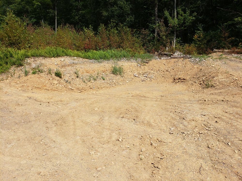 Cleared earth from land excavation with visible tire tracks and surrounding vegetation.