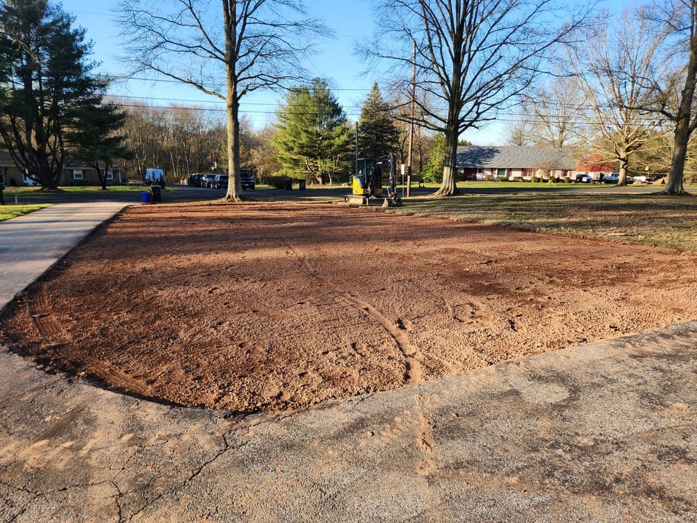Cleared and leveled dirt area ready for landscaping, surrounded by trees and residential homes.