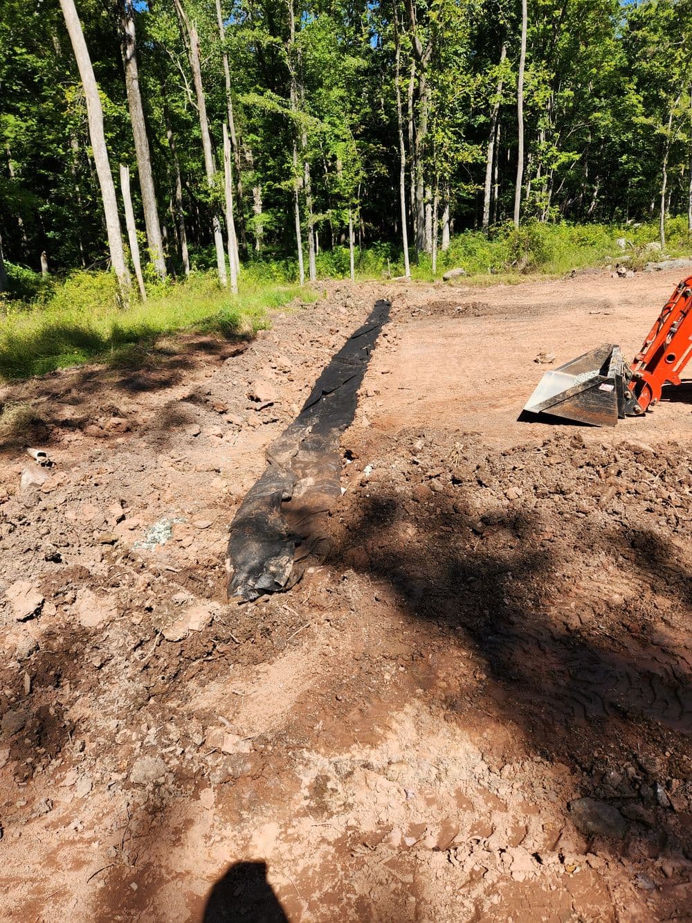 Excavated land with black plastic barrier in wooded area, ready for construction.