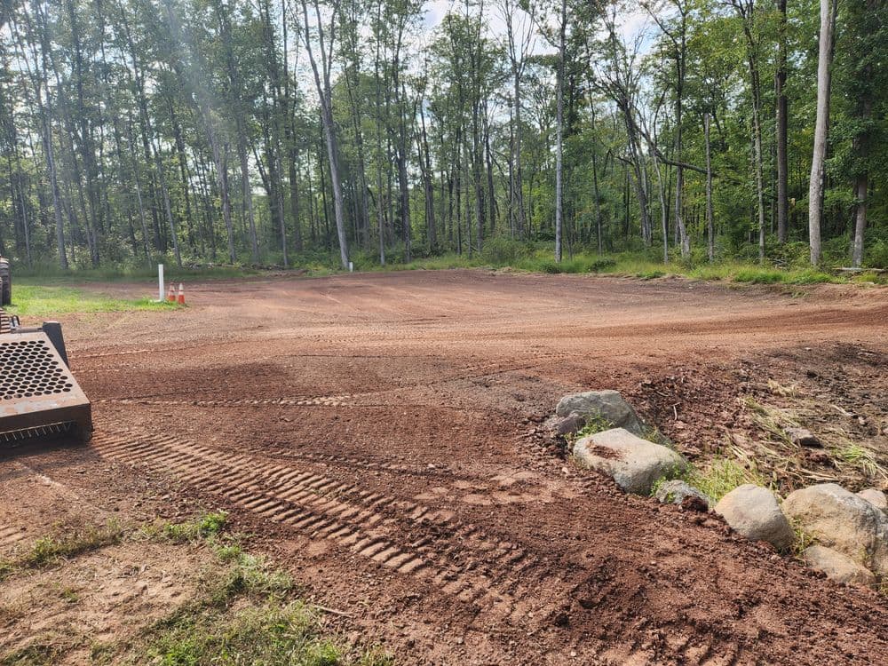 Cleared dirt area in a forested setting, ready for construction or landscaping.