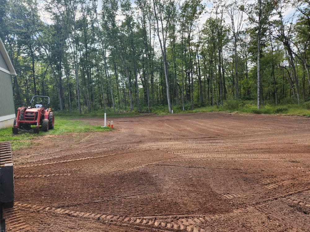 Tractor parked on freshly leveled dirt in a forested area with trees in the background.